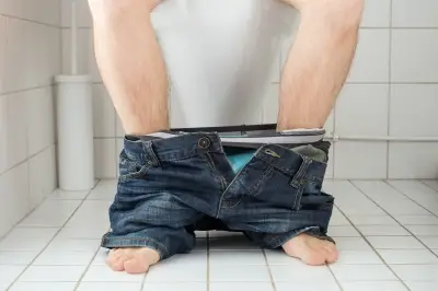man in small bathroom toilet with pants pulled down