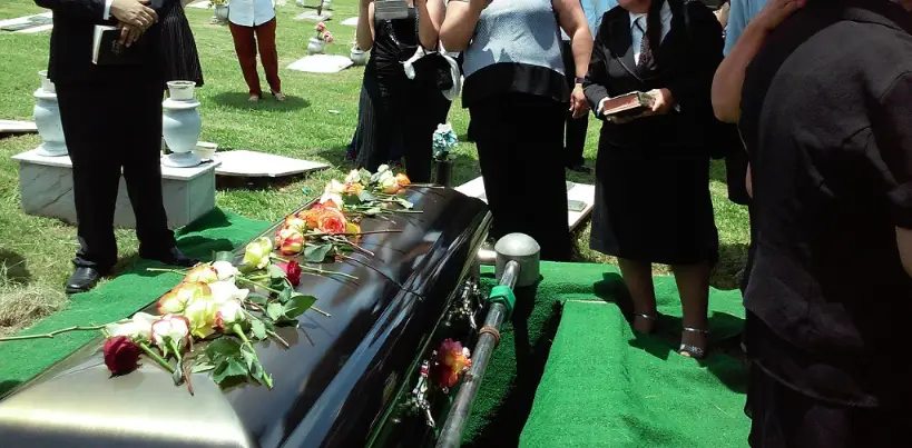 outdoor funeral at the cemetery with people dressed in black standing around the casket outdoor funeral
