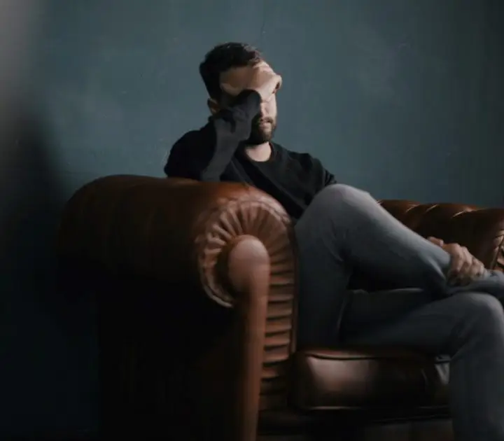 How To Reduce Financial Worries Once And For All. A man sitting on a leather couch in deep thought. 