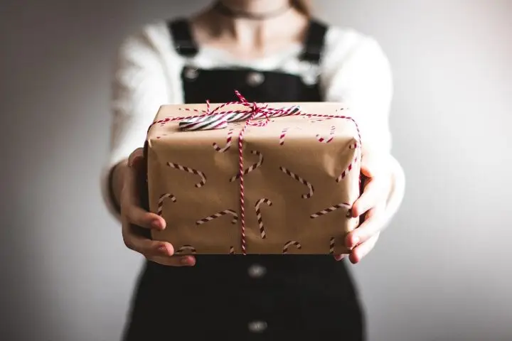 A woman holding out a Christmas Gift to someone,