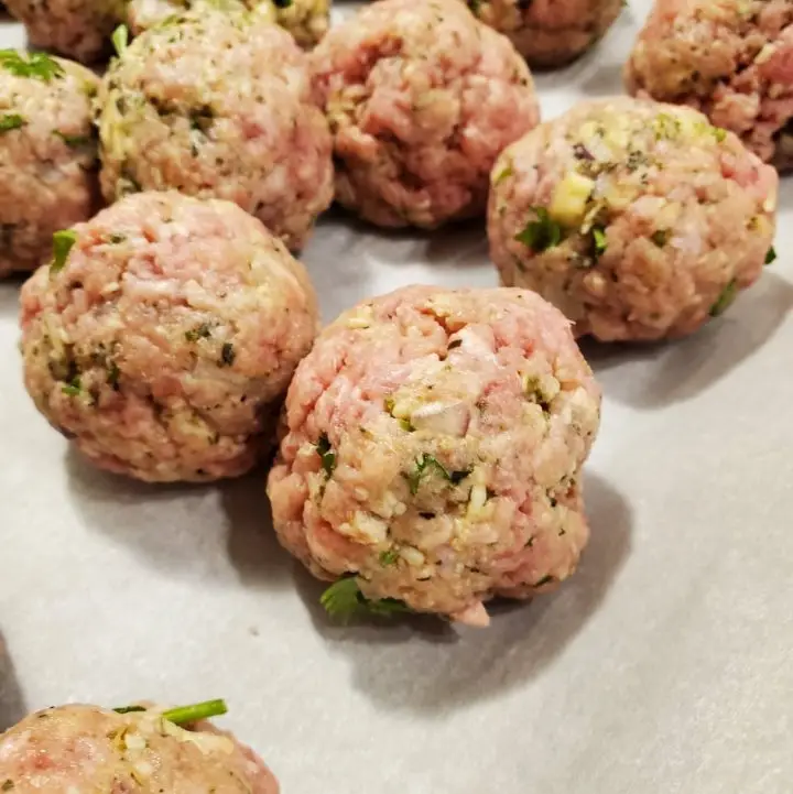 Raw Italian meatballs on a parchment-lined baking sheet