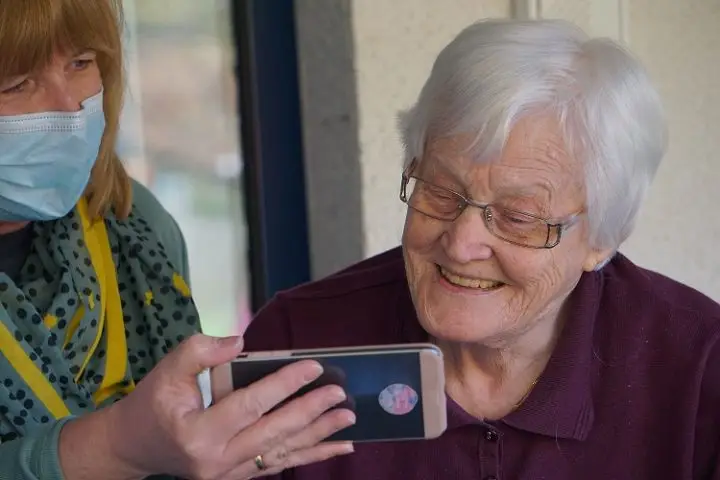 A daughter showing her mom photos on her mobile phone at a long-term care facility