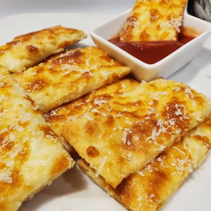 Keto Cheese Breadsticks topped with grated Parmigiano Reggiano cheese and served with marinara sauce.