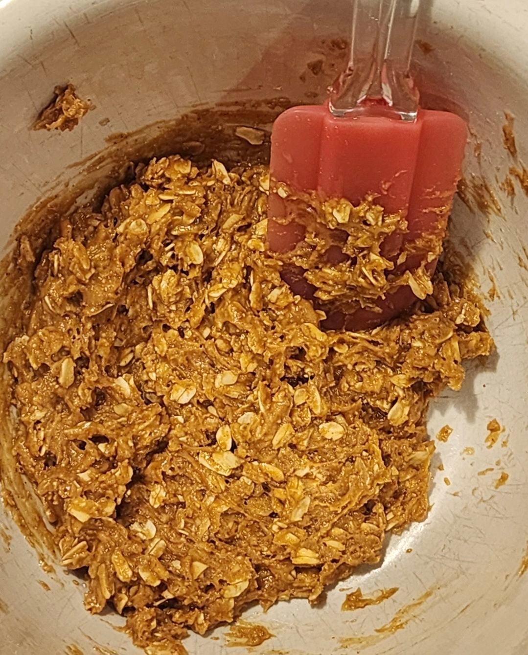 Thick homemade peanut butter oatmeal cookie dough mixed with a pink spatula in a bowl